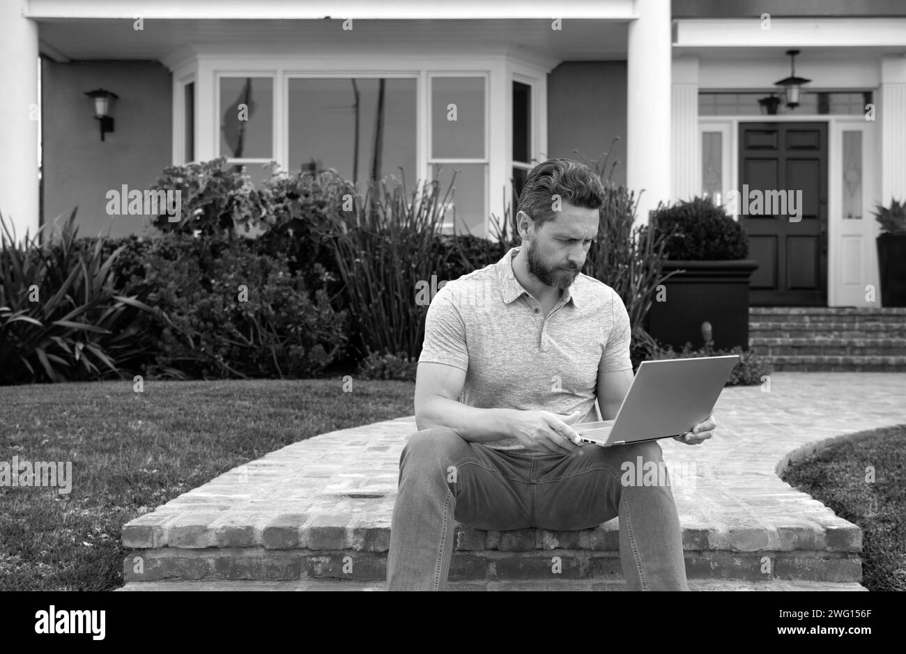 Beau jeune homme d'affaires assis sur les escaliers tout en utilisant son ordinateur portable. Jeune homme d'affaires à l'extérieur travail occupation style de vie Banque D'Images