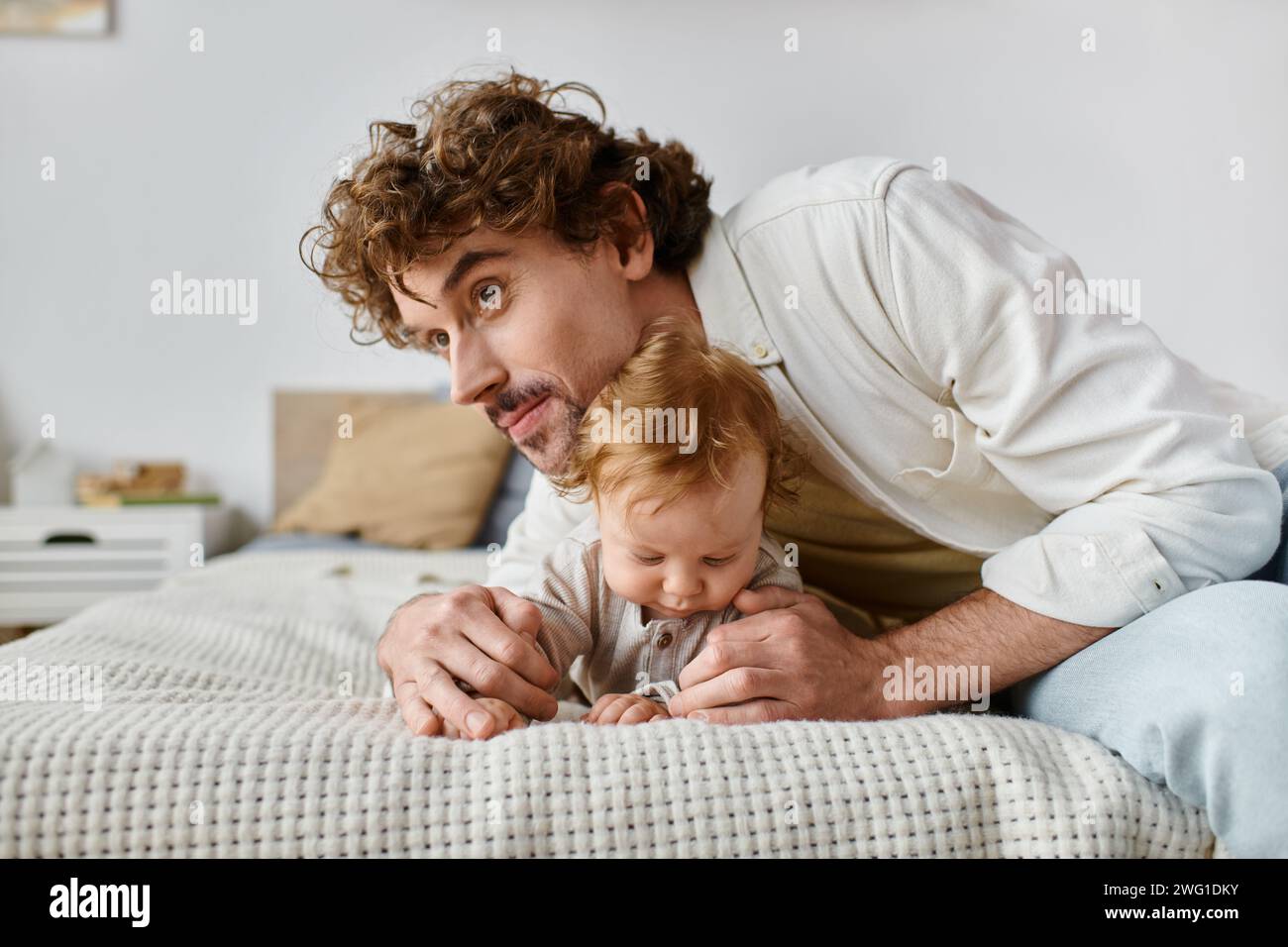 père protecteur avec les cheveux bouclés embrassant son bébé garçon tout en étant couché ensemble sur le lit, précieux Banque D'Images