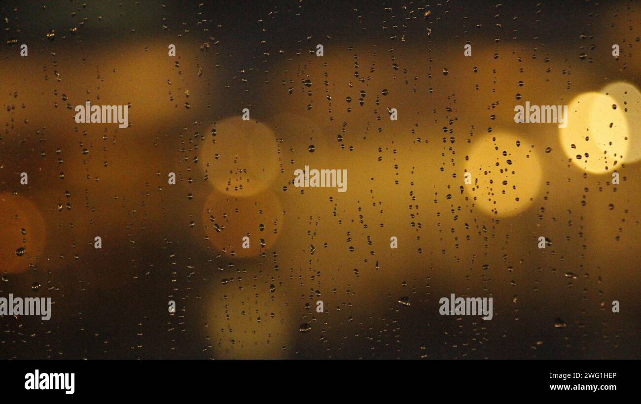 Une photo floue de gouttes de pluie sur une surface de verre avec une lumière chatoyante. Banque D'Images