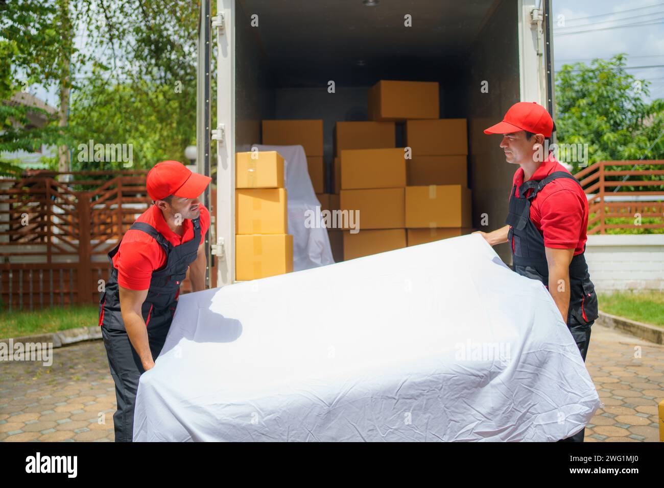Deux déménageurs d'entreprise masculins qui aident avec diligence à décharger un canapé de leur véhicule devant la maison d'un client Banque D'Images