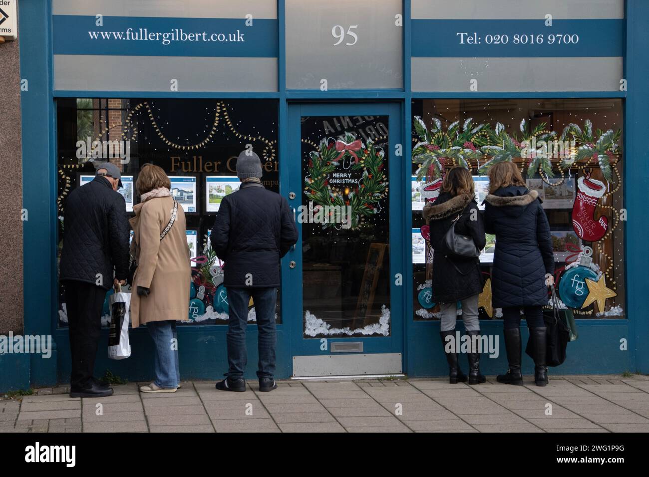 Les gens regardant les propriétés à travers un agent immobilier vitrine de la rue pendant la période de Noël, Wimbledon Village, Londres SW19, Angleterre. Banque D'Images