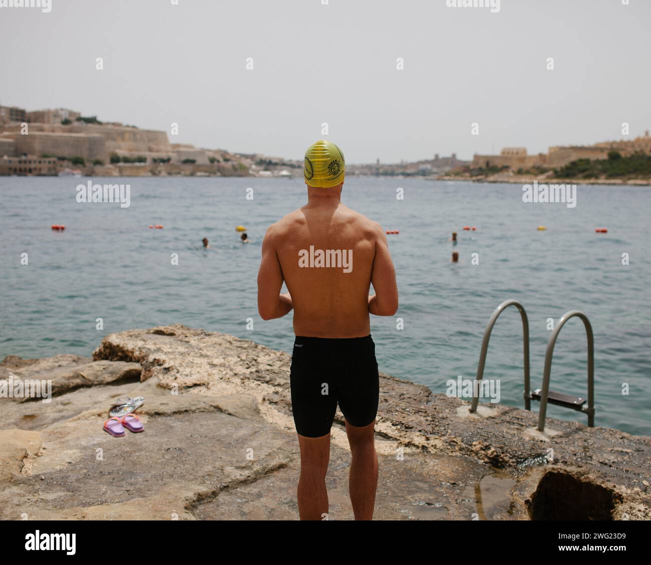 Un nageur se prépare à entrer dans la mer à la plage de Tigne point, Malte. La Valette peut être vue en arrière-plan. Banque D'Images