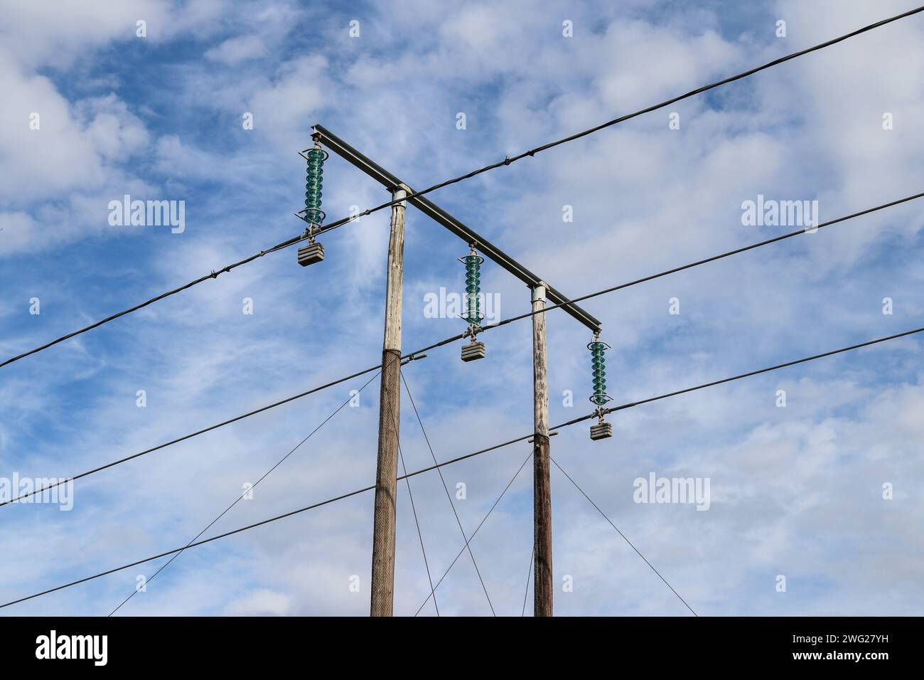 Trois câbles électriques à haute tension sur un poteau avec ciel bleu et nuages en arrière-plan Banque D'Images
