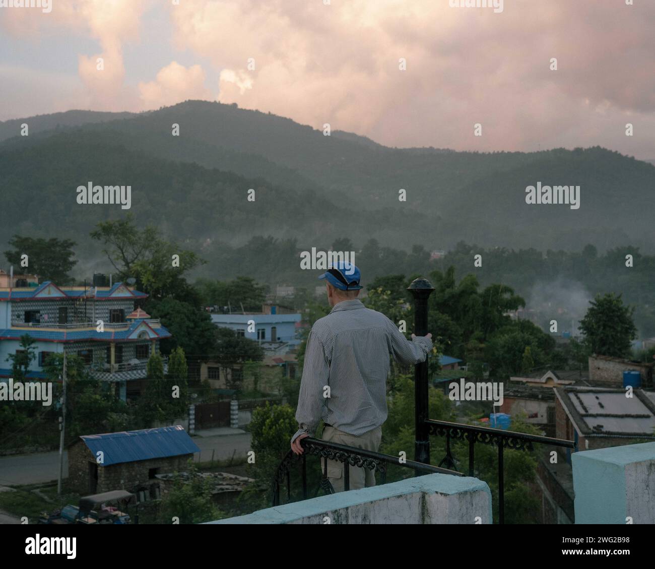 Un touriste portant une casquette bleue se tient sur un toit-terrasse donnant sur les montagnes à Birendranagar, province de Karnali, Népal. Banque D'Images