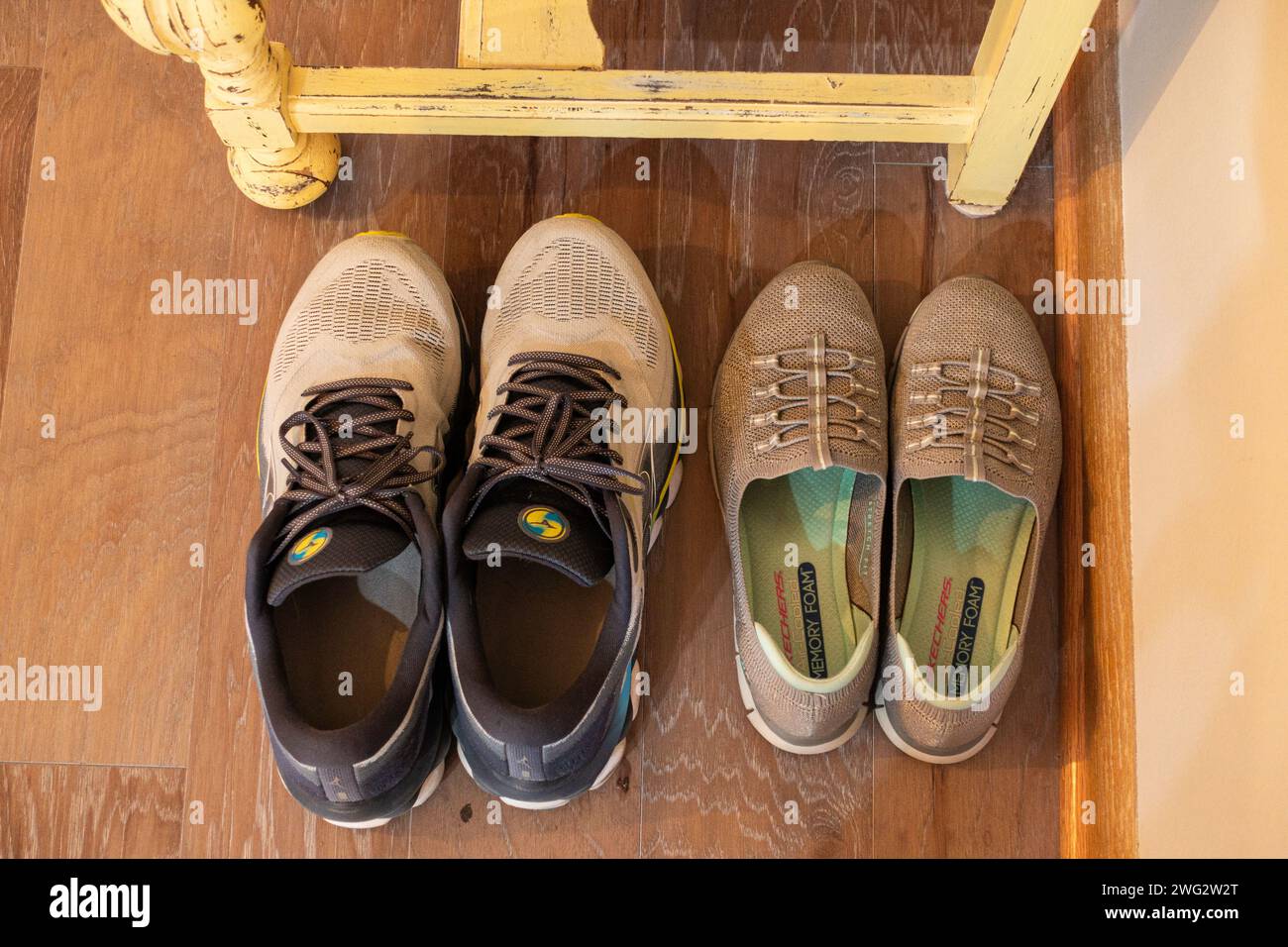 Une paire de chaussures de sport pour homme est assise côte à côte avec une paire de chaussures de sport Sketcher pour femme sur un plancher de bois franc. Regardant vers le bas. ÉTATS-UNIS Banque D'Images
