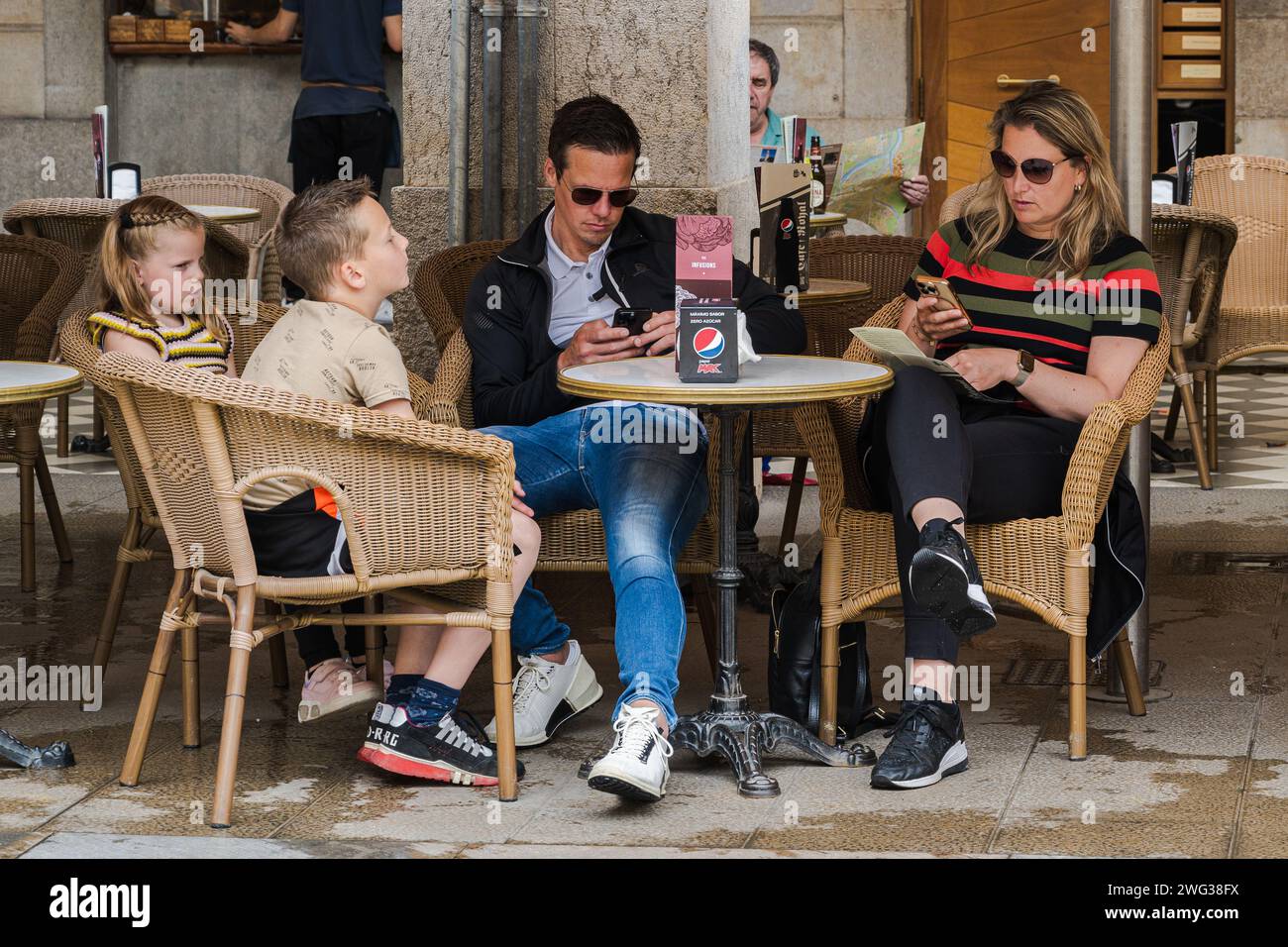 Gérone, Espagne — 31 mai 2023. Une famille s’arrête dans un café extérieur à Gérone ; les parents vérifient leurs téléphones portables pendant que les enfants attendent. Banque D'Images