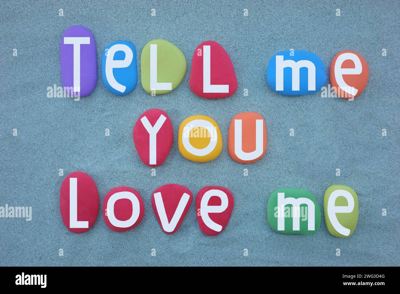 Dites-moi que vous m'aimez, phrase d'amour créative composée de lettres de pierre multicolores sur du sable vert Banque D'Images