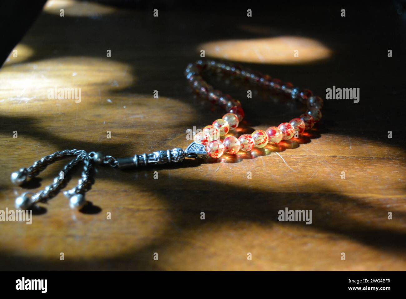 Perles religieuses musulmanes de perles jaunes et rouges sur une table en bois laqué de style ancien éclairée par les rayons du soleil Banque D'Images