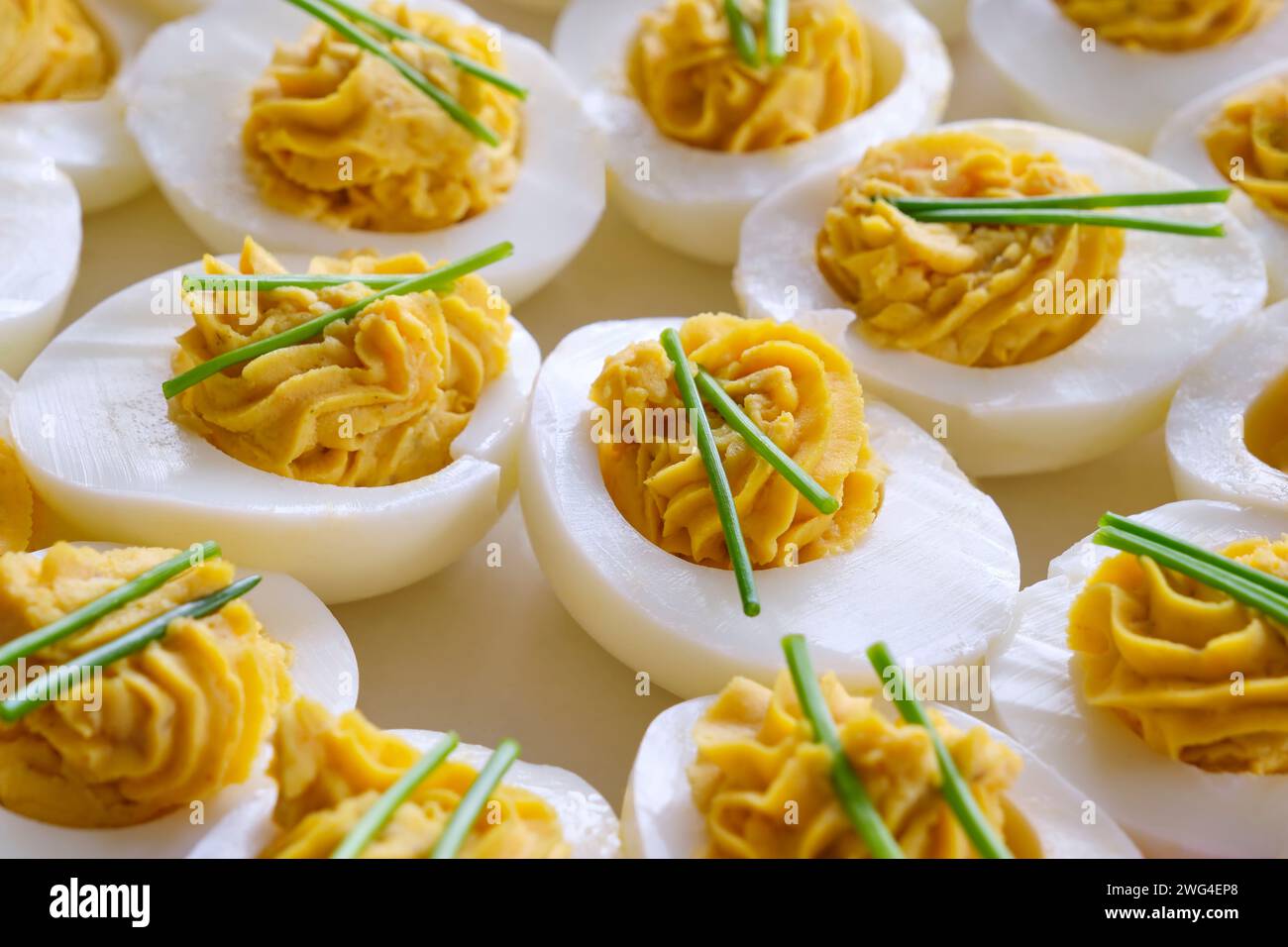 Gros plan d'œufs farcis avec deux brins de ciboulette sur une assiette blanche sur une table en bois. Banque D'Images