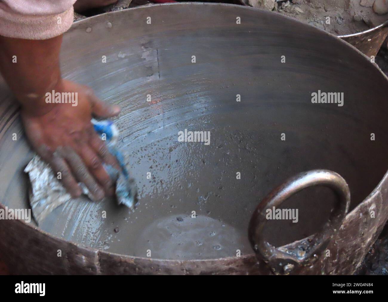 Une photo de mouvement d'action d'un homme nettoyant une grande marmite de cuisson avec du sable et du gravier avec un chiffon sale et de l'eau. Cuisine manger dehors concept d'hygiène Banque D'Images