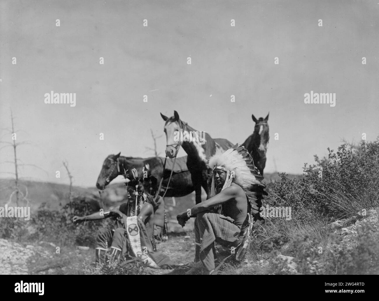 The Talk, c1905. Trois Crow hommes, assis dans une zone rocheuse avec des arbustes à faible croissance, leurs chevaux se reposent à proximité. Banque D'Images The Talk, c1905. Trois Crow hommes, assis dans une zone rocheuse avec des arbustes à faible croissance, leurs chevaux se reposent à proximité. Banque D'Images