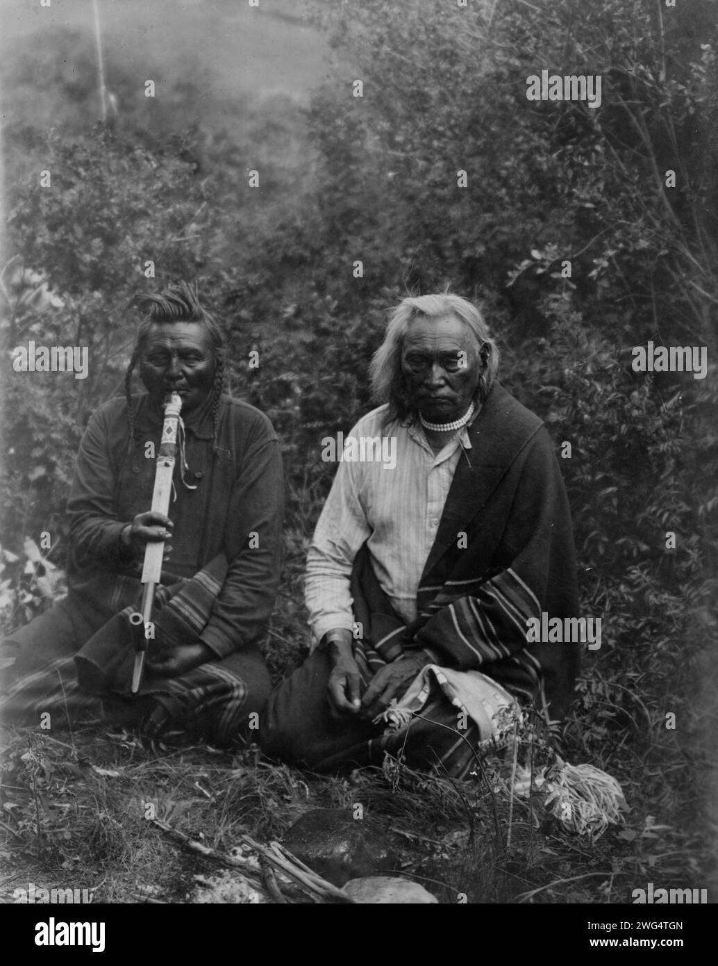 Une fumée, c1905. Deux Indiens Crow dans le Montana, assis par terre, l'un fume une pipe. Banque D'Images Une fumée, c1905. Deux Indiens Crow dans le Montana, assis par terre, l'un fume une pipe. Banque D'Images