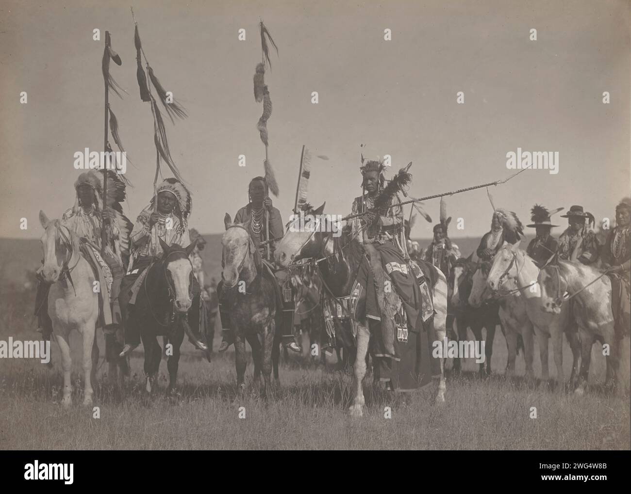 Victoire, 1908. La photographie montre plusieurs Indiens Crow, dont Plenty coups, Wet, Bull Don't Fall Down et Spotted Jack Rabbit portant des vêtements et coiffes traditionnels alors qu'ils transportaient des bâtons à cheval. Banque D'Images Victoire, 1908. La photographie montre plusieurs Indiens Crow, dont Plenty coups, Wet, Bull Don't Fall Down et Spotted Jack Rabbit portant des vêtements et coiffes traditionnels alors qu'ils transportaient des bâtons à cheval. Banque D'Images