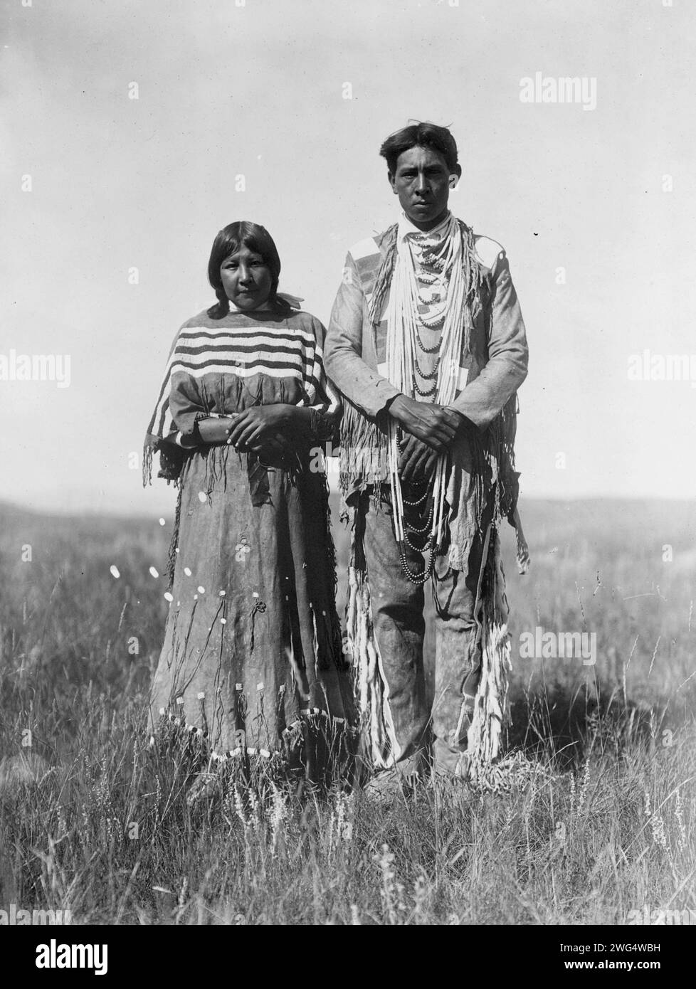 Joe Russell, c1910. Piegan homme et femme debout dans la prairie ouverte. Banque D'Images