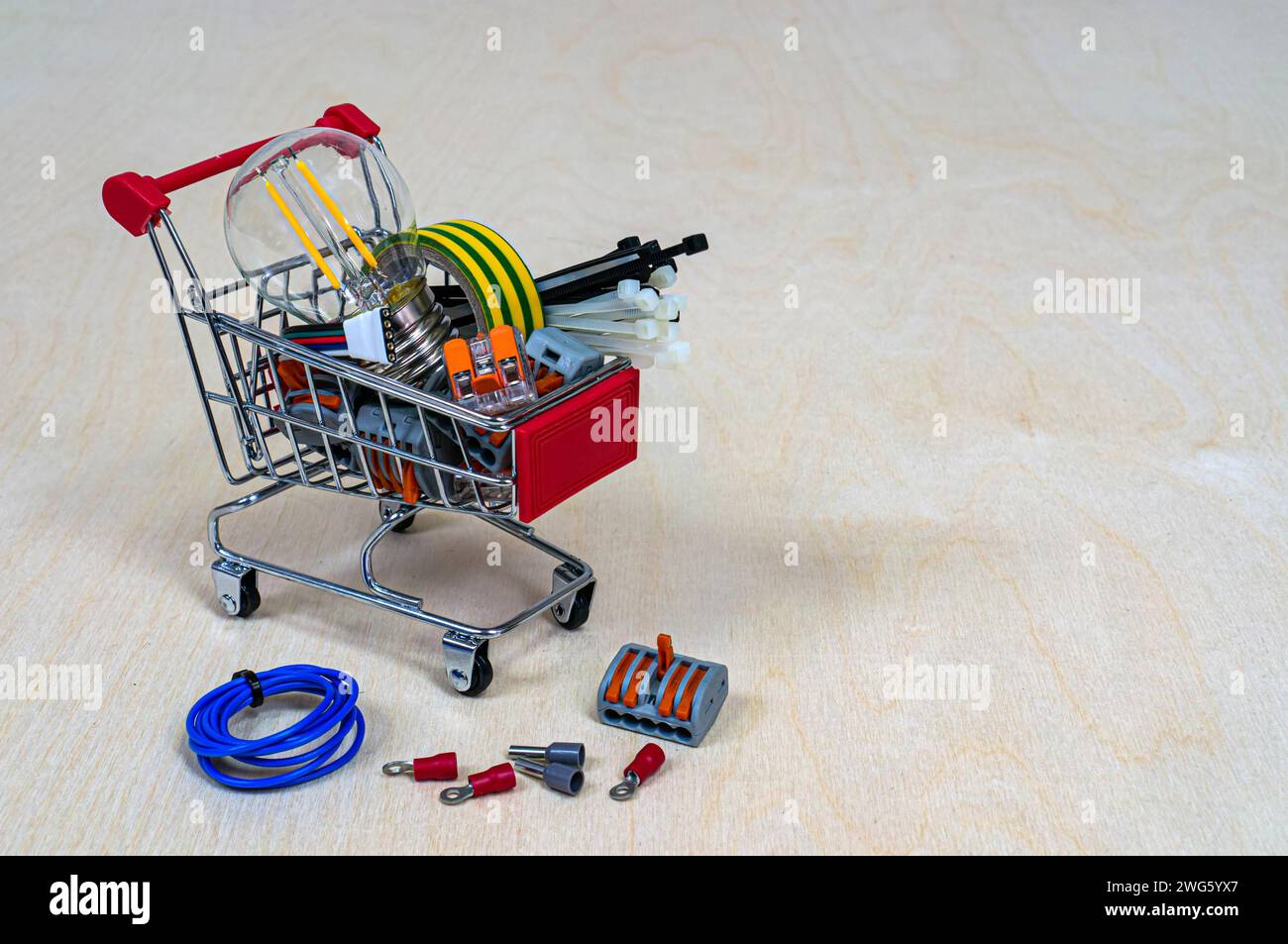 Un panier avec pièces et composants électriques. Bornes, ampoule, ruban isolant, serre-câbles. Concept : magasin de produits électriques. Dos en bois Banque D'Images