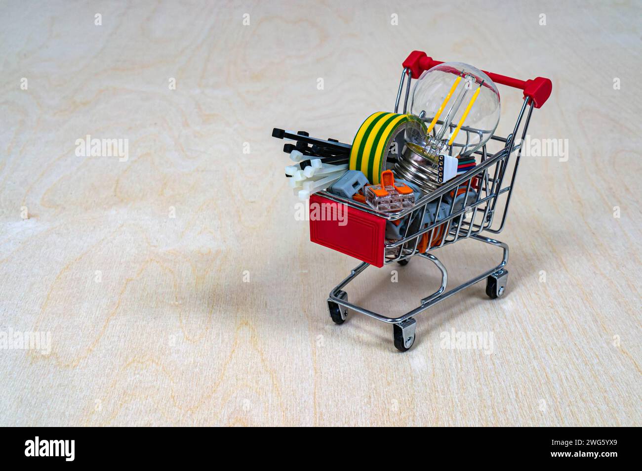 Un panier avec pièces et composants électriques. Bornes, ampoule, ruban isolant, serre-câbles. Concept : magasin de produits électriques. Dos en bois Banque D'Images