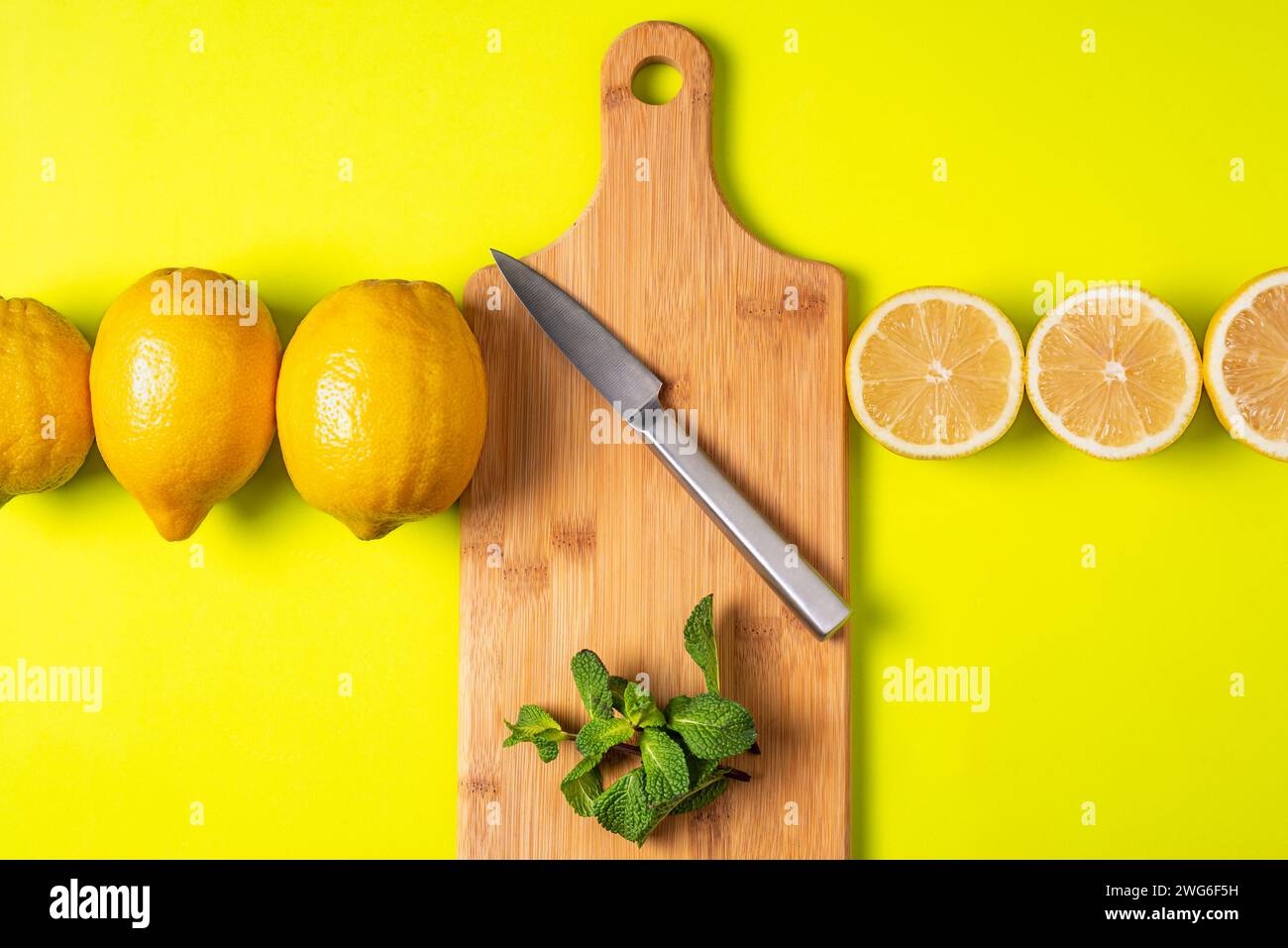 Planche à découper avec un couteau et de la menthe, avec une rangée de citrons entiers d'un côté et la moitié de citrons de l'autre. Banque D'Images