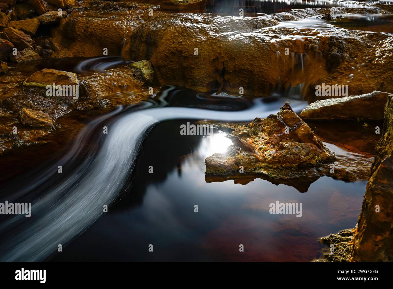 Gros plan de tapis microbiens orange au-dessus des eaux sombres du Rio Tinto, mettant en valeur les contrastes naturels Banque D'Images