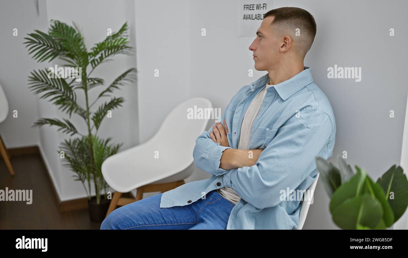 Un jeune homme hispanique contemplatif est assis dans une salle d'attente intérieure moderne avec les bras croisés. Banque D'Images