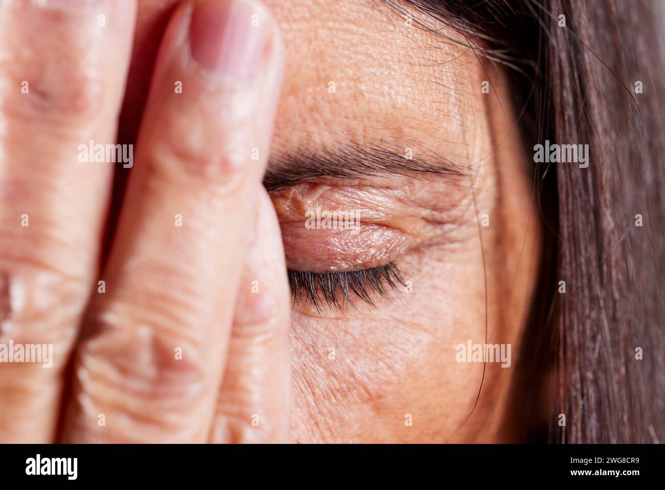 Gros plan d'une femme mature avec sa main couvrant la moitié de son visage avec l'œil fermé Banque D'Images