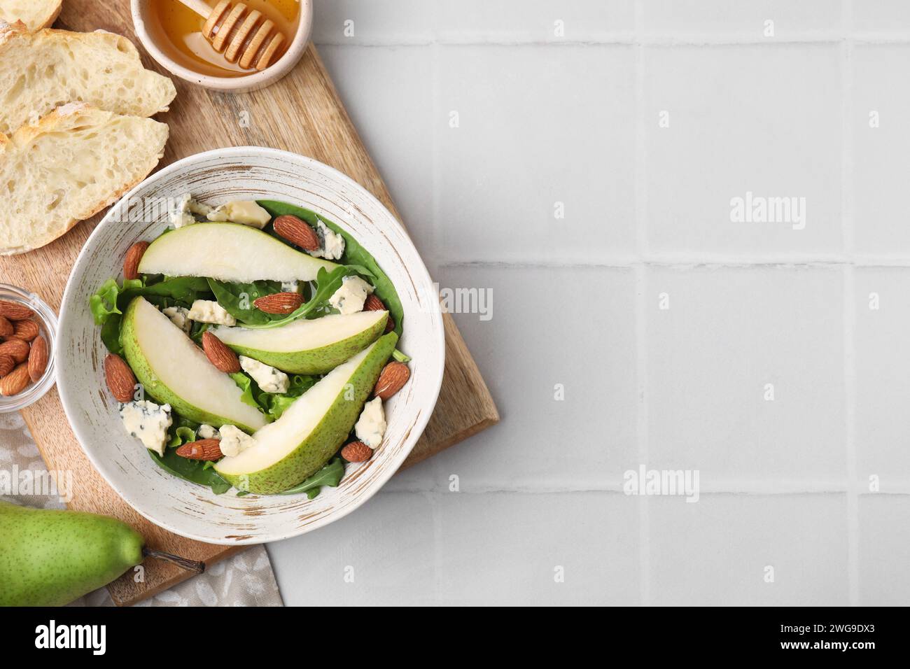 Délicieuse salade de poires dans un bol et produits sur une table carrelée légère, vue de dessus. Espace pour le texte Banque D'Images