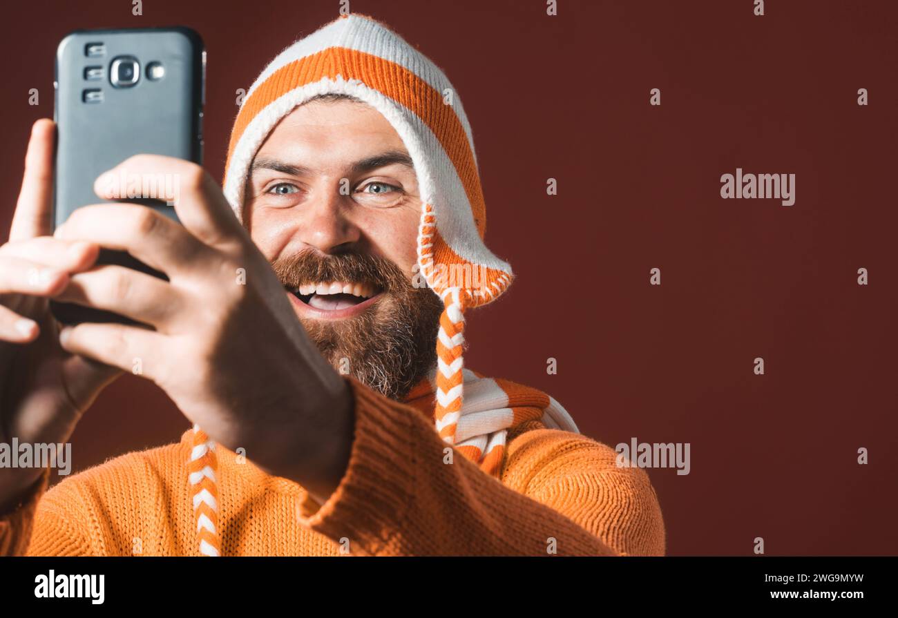 Homme barbu en chapeau drôle prenant selfie avec son smartphone. Hobby photographe. Durée du selfie. Homme joyeux fait autoportrait sur téléphone intelligent. Beau Banque D'Images