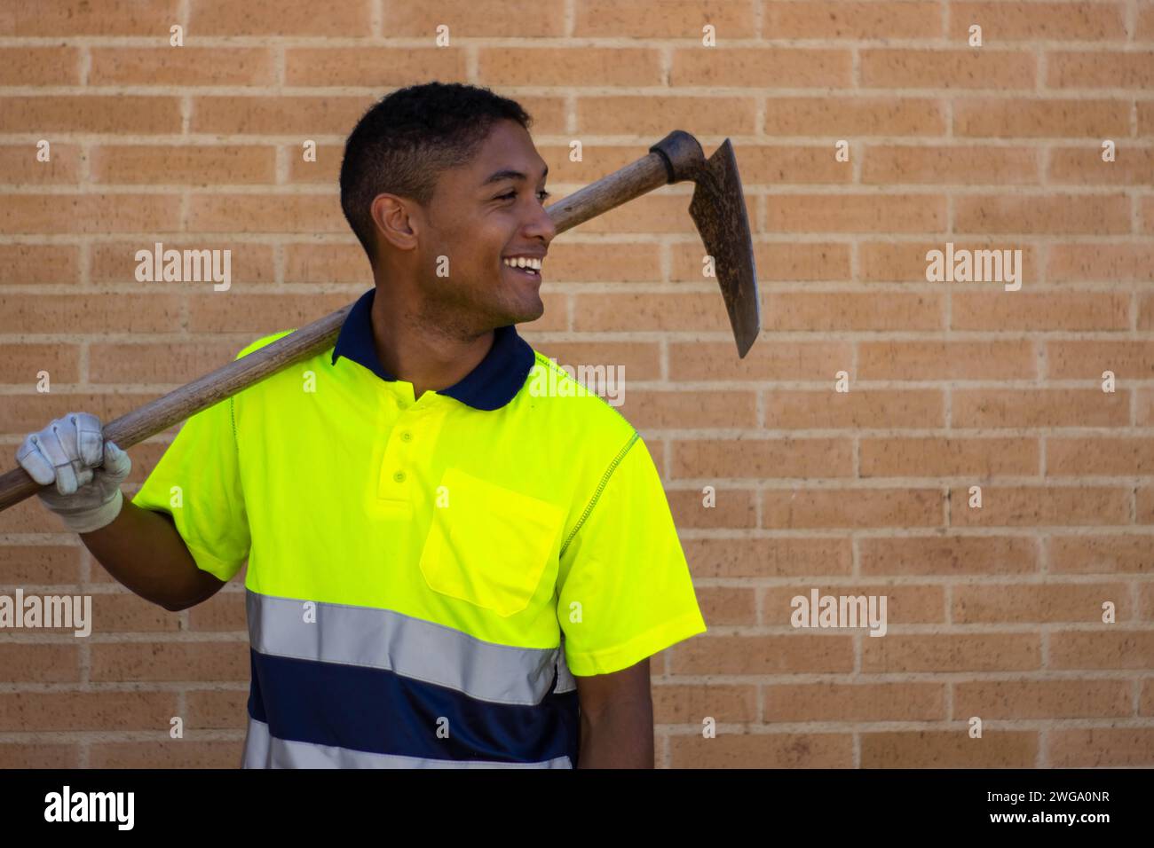 Portrait d'un ouvrier souriant avec une houe sur son épaule, mur de briques sur le fond Banque D'Images
