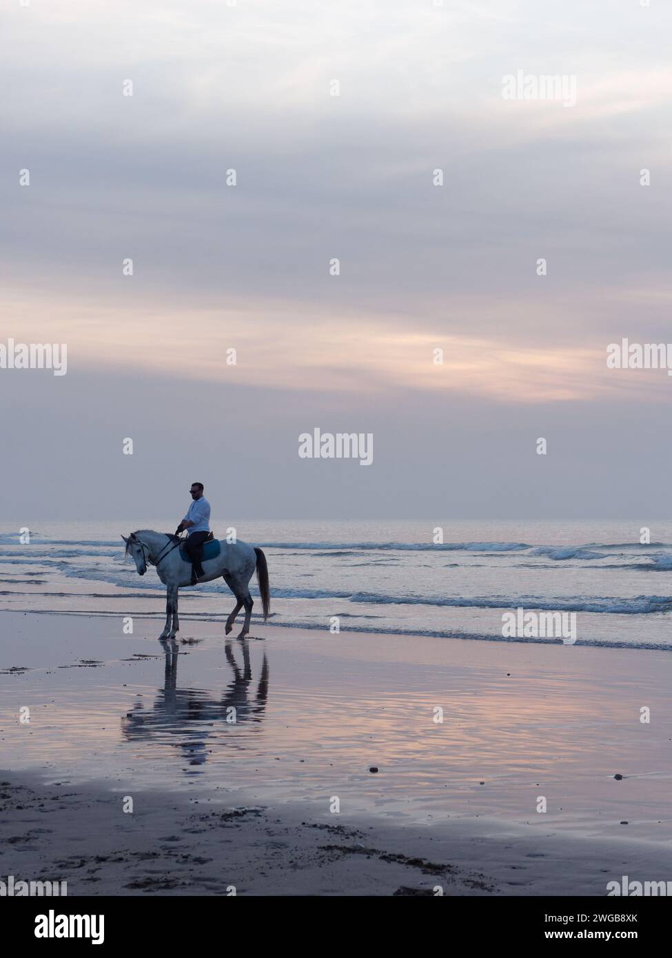 Cavalier à cheval sur une plage de sable au coucher du soleil à Essaouira, Maroc, le 3 février 2024 Banque D'Images