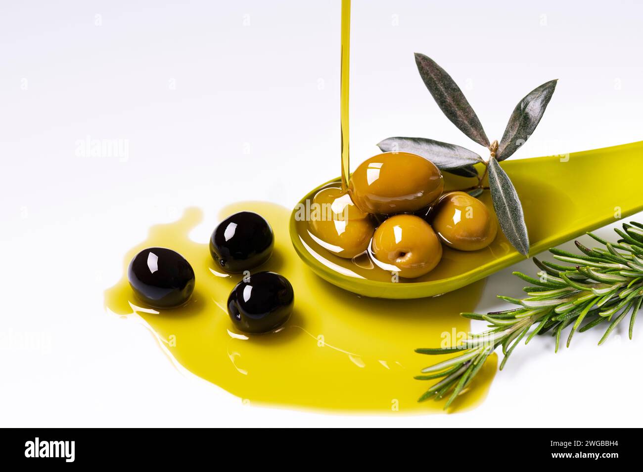au premier plan, un filet d'huile d'olive extra vierge est versé dans une louche verte avec des olives aromatisées au romarin Banque D'Images