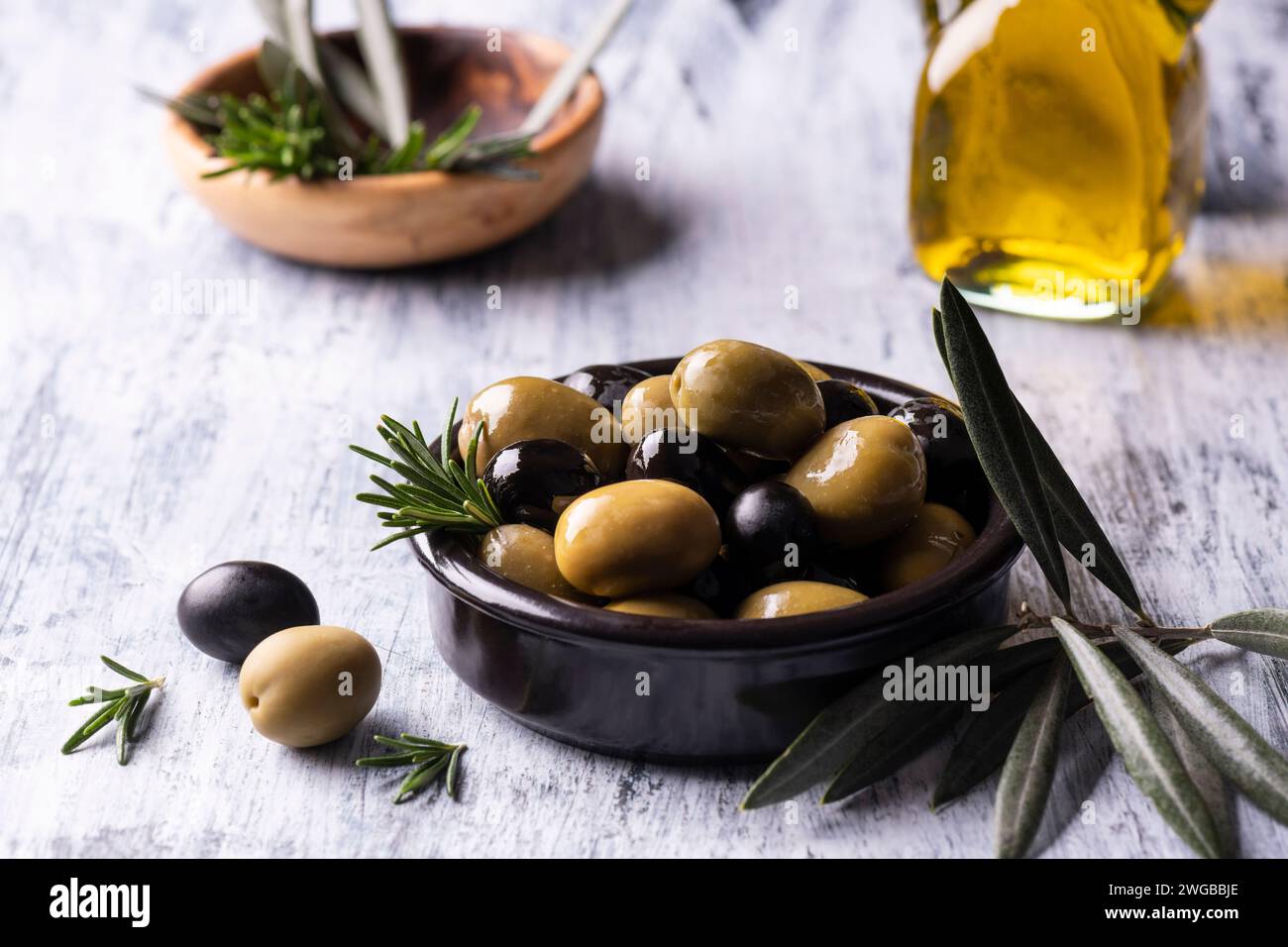 au premier plan un bol noir avec des olives mélangées aromatisées au romarin avec de l'huile d'olive extra vierge Banque D'Images