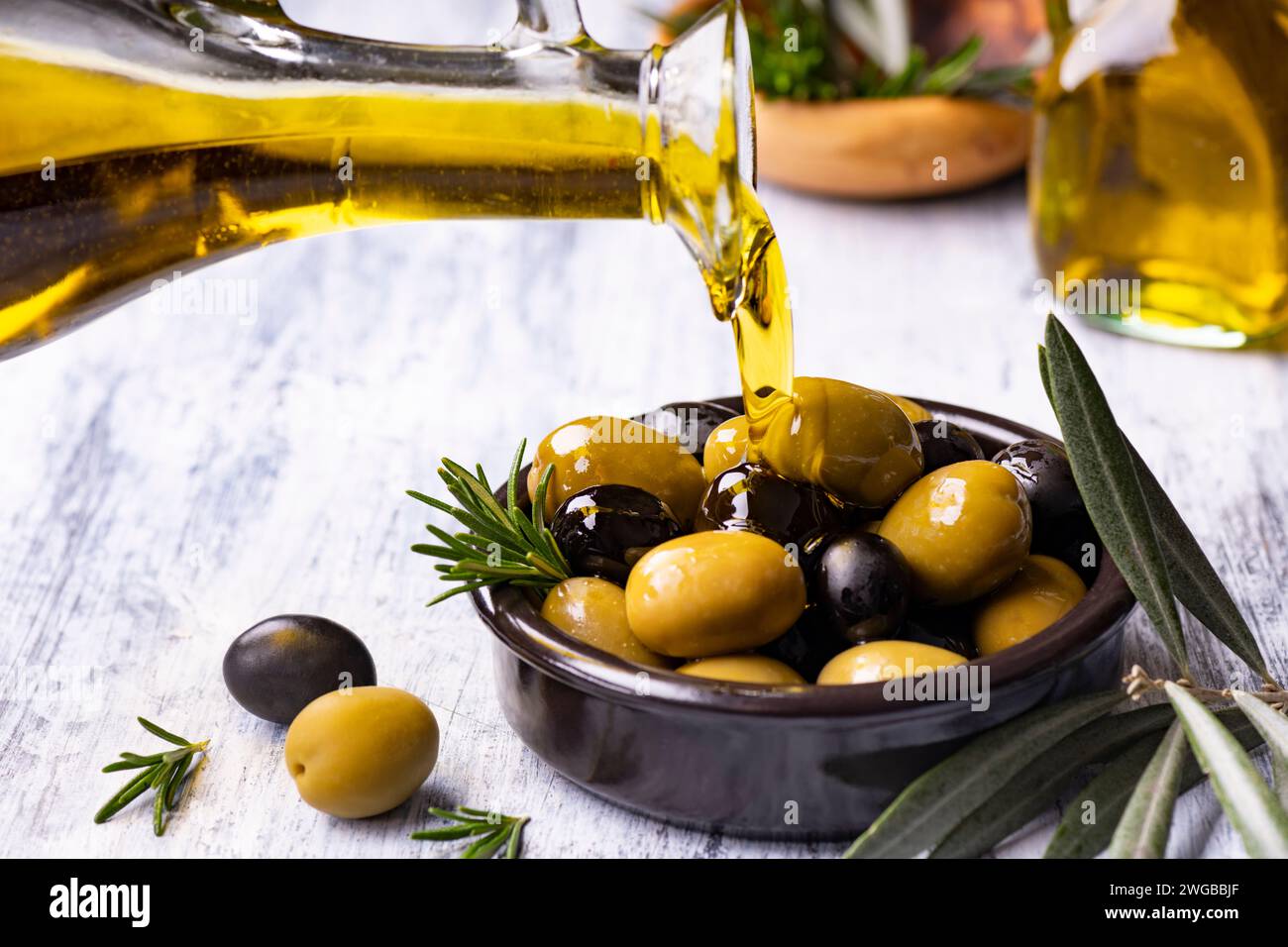 au premier plan, de l'huile d'olive extra vierge est versée dans un bol avec des olives aromatisées au romarin Banque D'Images