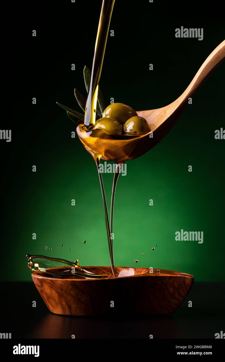 de la cuillère en bois, au premier plan, l'huile d'olive extra vierge est versée dans un bol en bois d'olivier avec des olives Banque D'Images