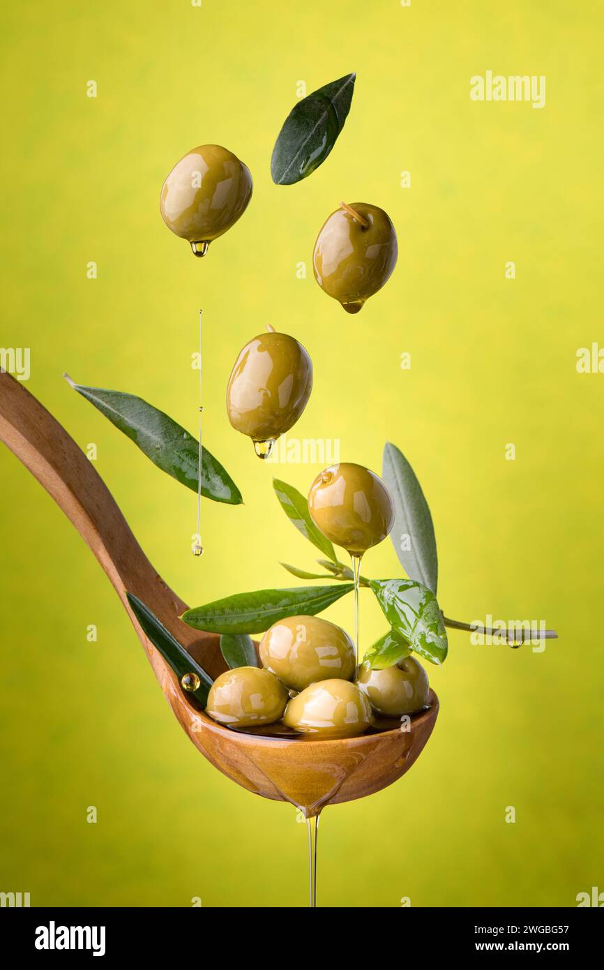 louche avec des olives et de l'huile sur un fond vert. Les olives, l’huile d’olive extra vierge et les feuilles d’olive flottent dans l’air Banque D'Images