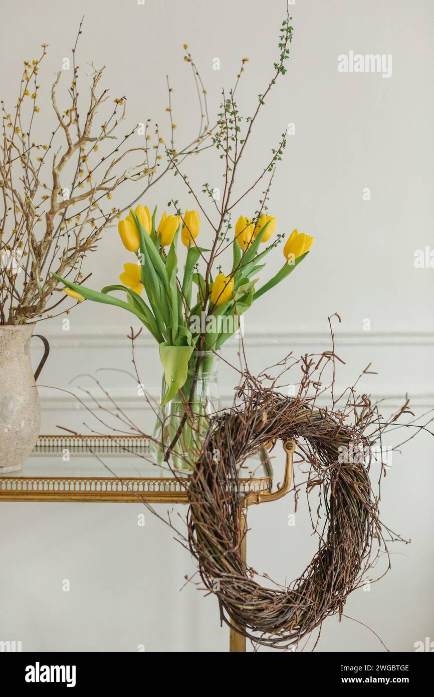 Gros plan d'un bouquet de tulipes jaunes dans un vase sur une table avec une couronne rustique et une cruche avec des branches Banque D'Images