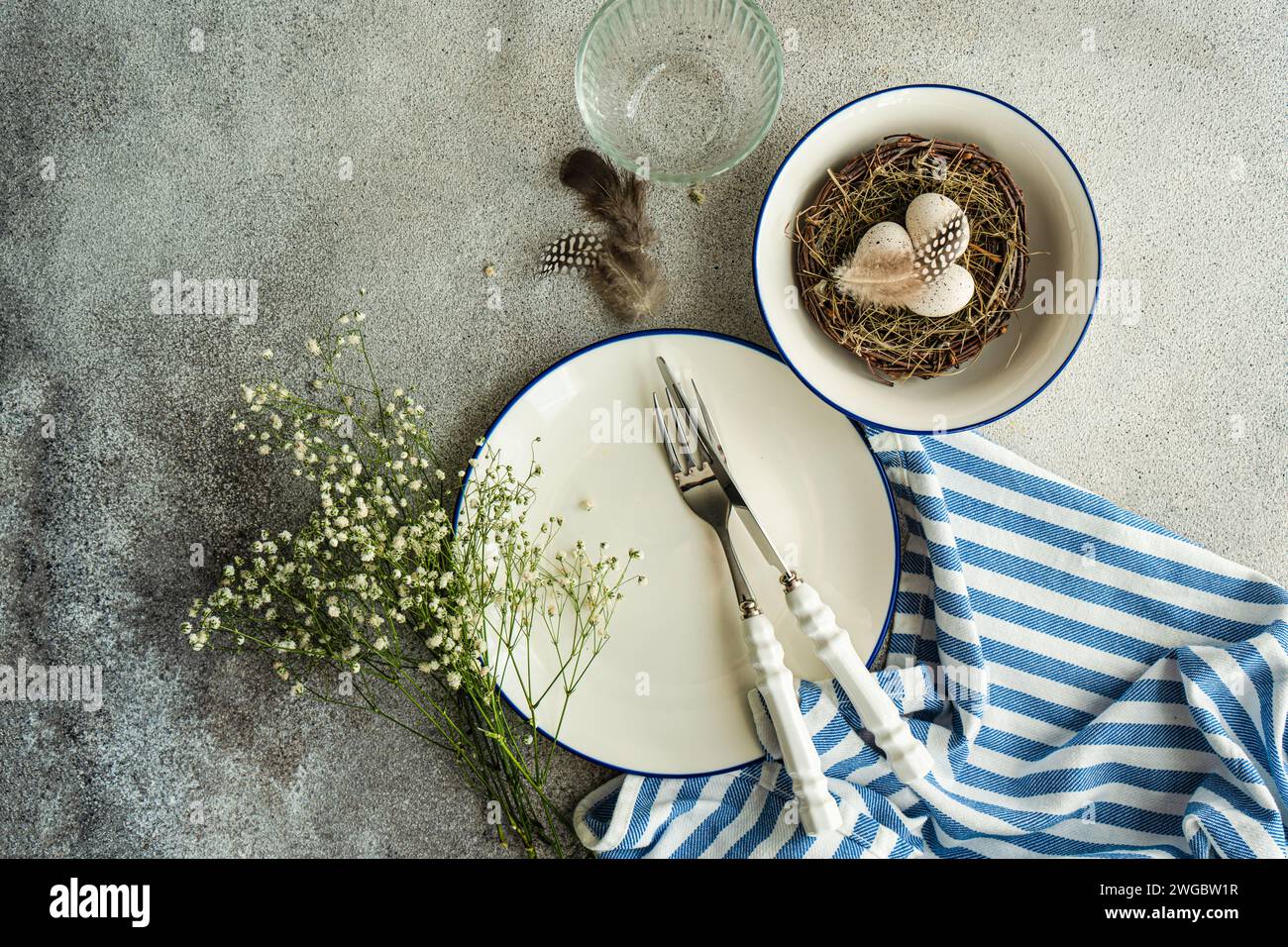 Vue aérienne d'un lieu de Pâques avec des fleurs blanches de gypsophila et un nid d'oiseau avec des œufs de Pâques peints et des plumes Banque D'Images