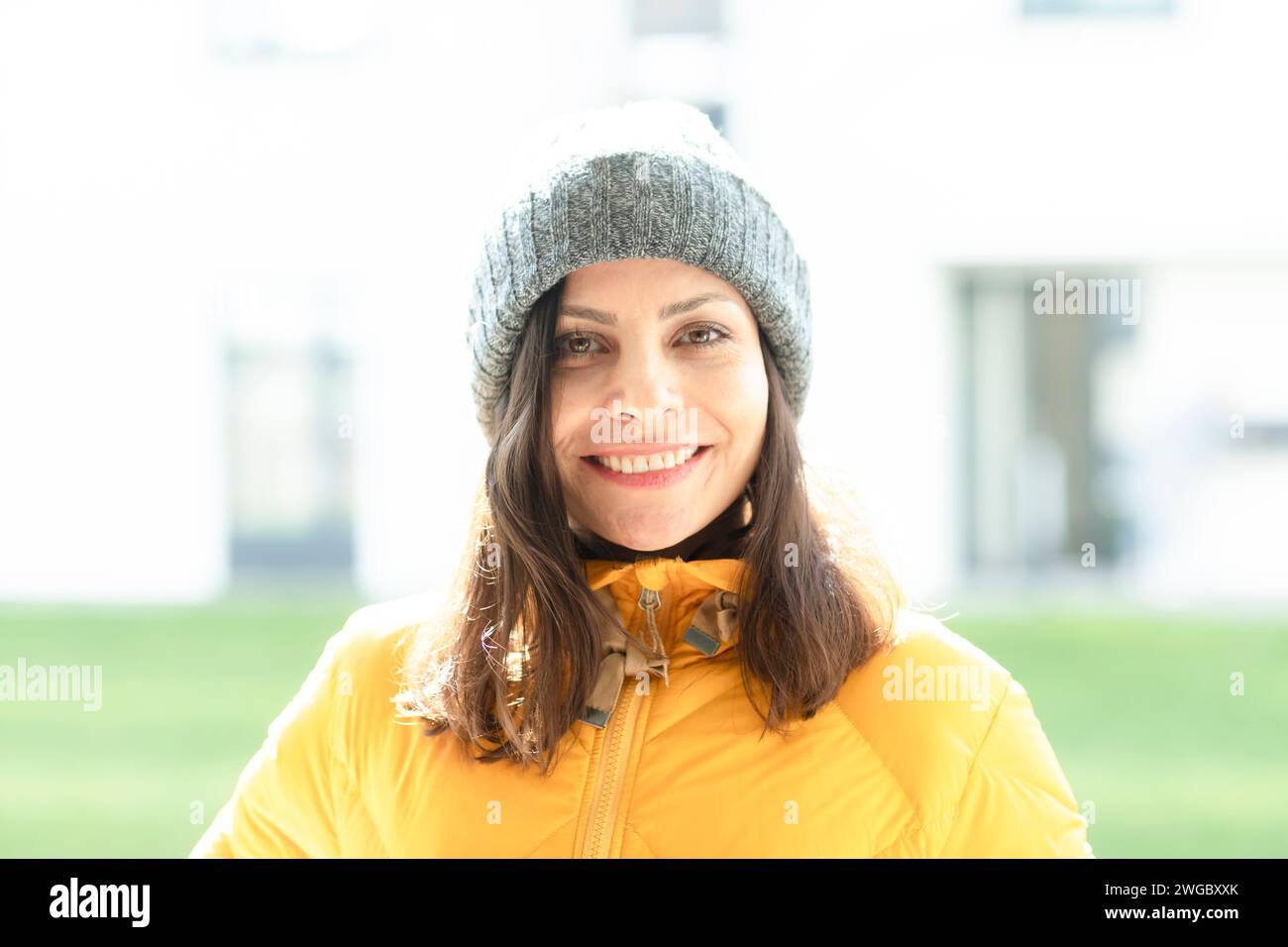 Portrait d'une femme souriante dans un chapeau laineux et un manteau gonflant debout devant un immeuble résidentiel, Allemagne Banque D'Images