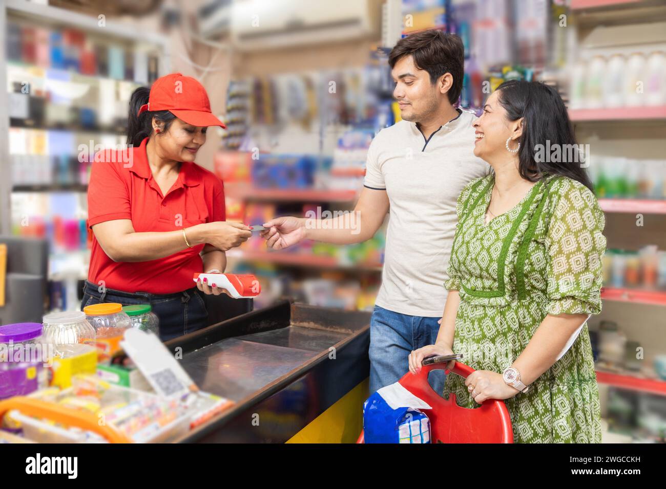 Couple indien à l'épicerie ou au supermarché en utilisant une carte de crédit ou de débit pour le paiement numérique. caissière indienne femelle prenant la carte pour le paiement digital in Banque D'Images