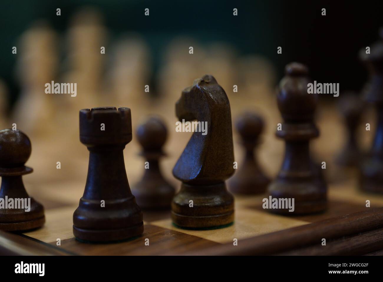 Des pièces d'échecs noires et blanches disposées sur une table en bois, juxtaposées contre un mur Banque D'Images