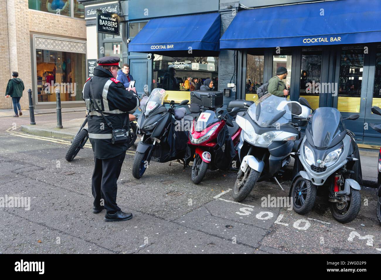 Un gardien de parking délivrant un avis de pénalité pour les motos garées à l'extérieur d'une zone désignée marquée dans la ville de Londres Angleterre Royaume-Uni Banque D'Images
