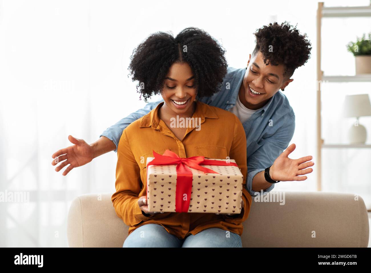 Une femme assise sur un canapé exprime une surprise ravie, les mains tendues Banque D'Images