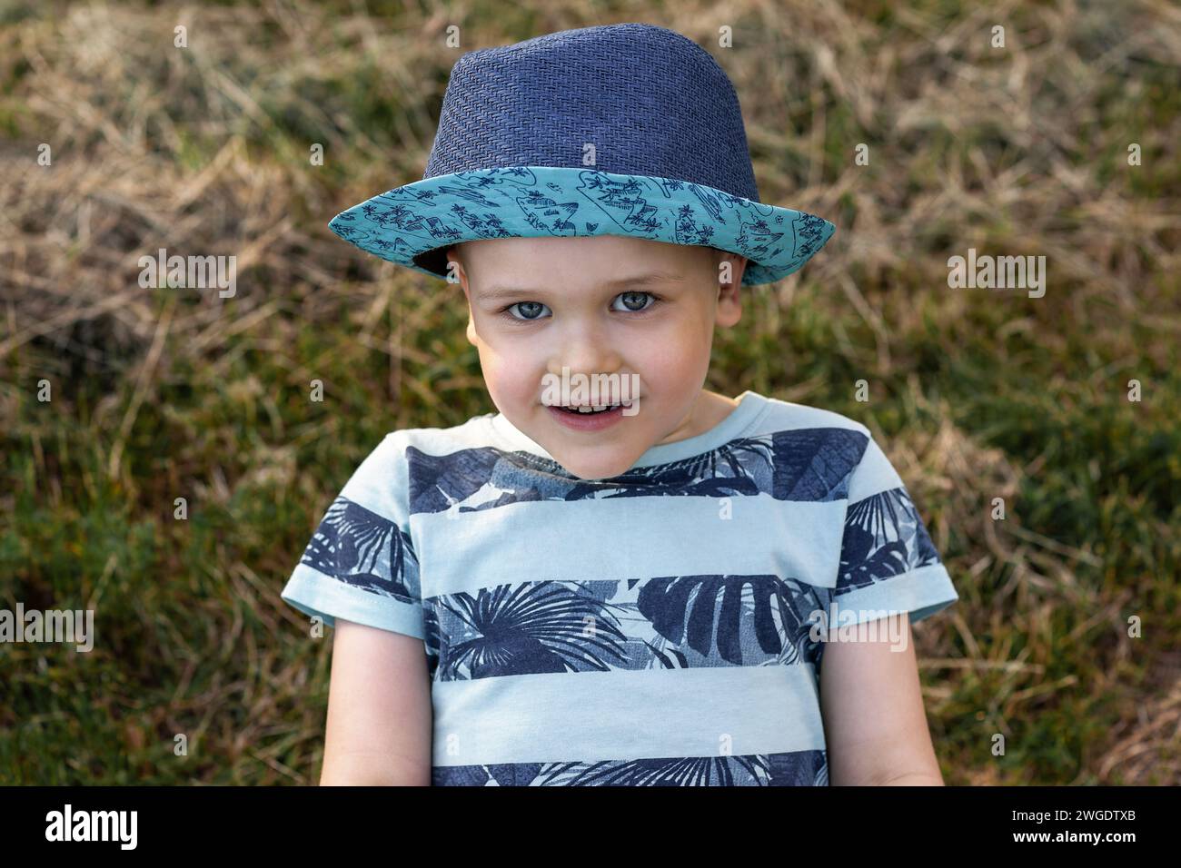Portrait d'un garçon caucasien joyeux dans un chapeau bleu sur un fond d'herbe sèche. Banque D'Images