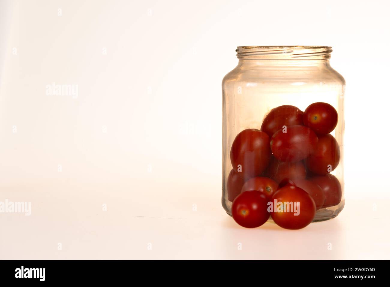 tomates prunes dans un pot en verre, deux tomates hors du pot sur fond blanc Banque D'Images