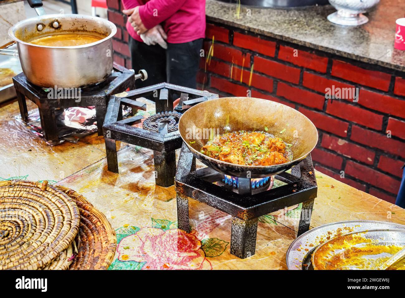 La nourriture étant préparée sur de simples cuisinières à gaz dans un restaurant typiquement pakistanais, herbes et épices déposées dans une casserole en acier avec un plat chaud, détail de gros plan Banque D'Images