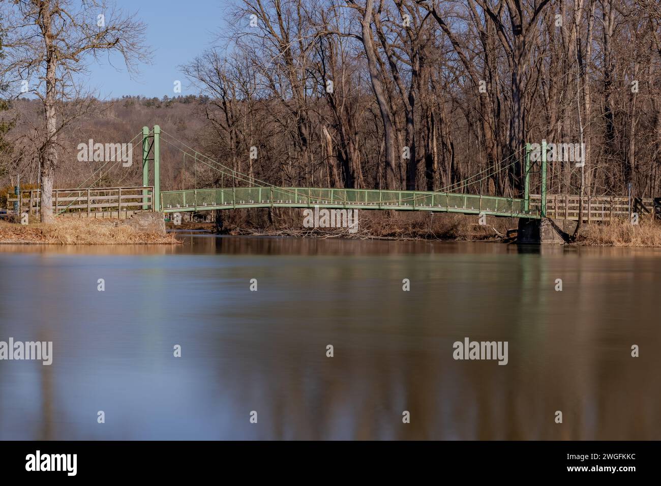 Photo hivernale du pont suspendu vert avec des arbres et des feuilles dans le parc Stewart à l'extrémité sud du lac Cayuga, Ithaca New York. Banque D'Images