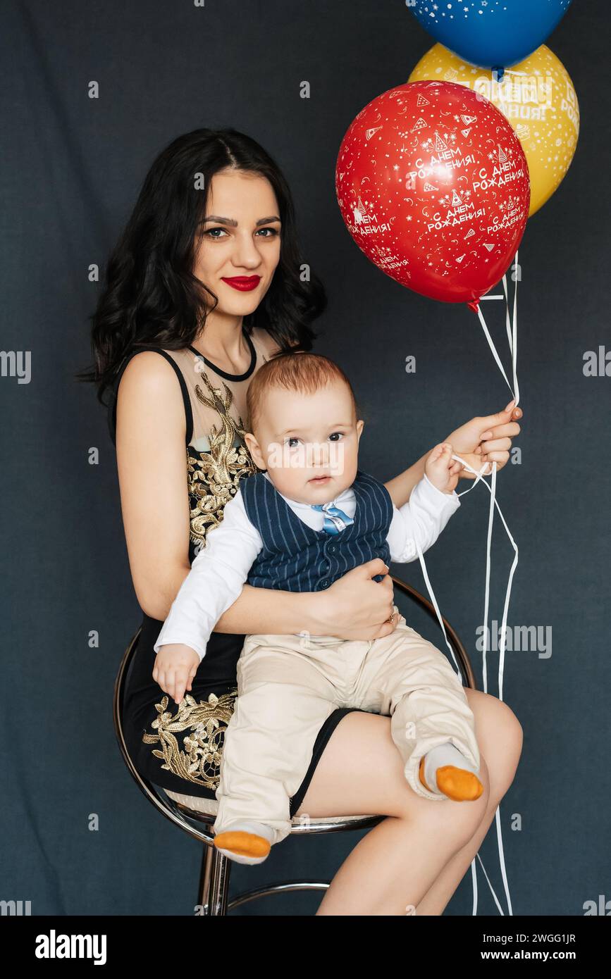 Jeune fille maman avec garçon bébé fils dans ses bras avec des ballons pour la fête d'anniversaire dans Studio. Ça dit joyeux anniversaire sur les ballons Banque D'Images