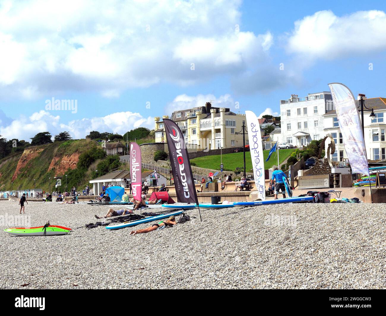 Touristes et planches de paddle sur la plage avec les bâtiments de la ville à l'arrière, Seaton, Devon, Royaume-Uni, Europe. Banque D'Images