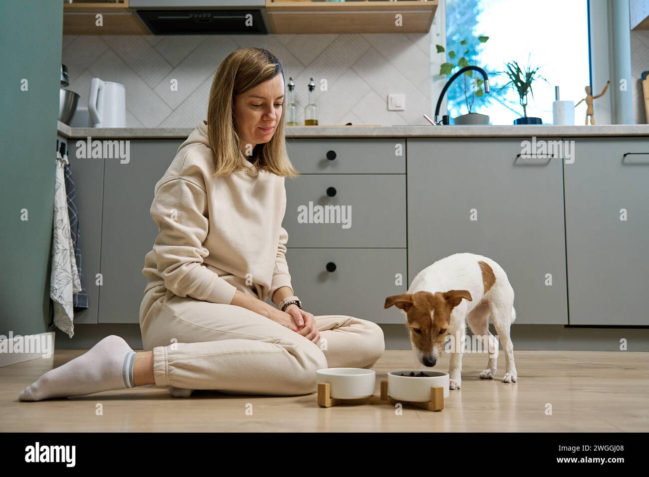 Femme mettant le bol de nourriture avec la nourriture pour son chien sur le sol dans la cuisine, propriétaire femme passant du temps avec l'animal de compagnie à la maison, alimentation animale et animal CA Banque D'Images