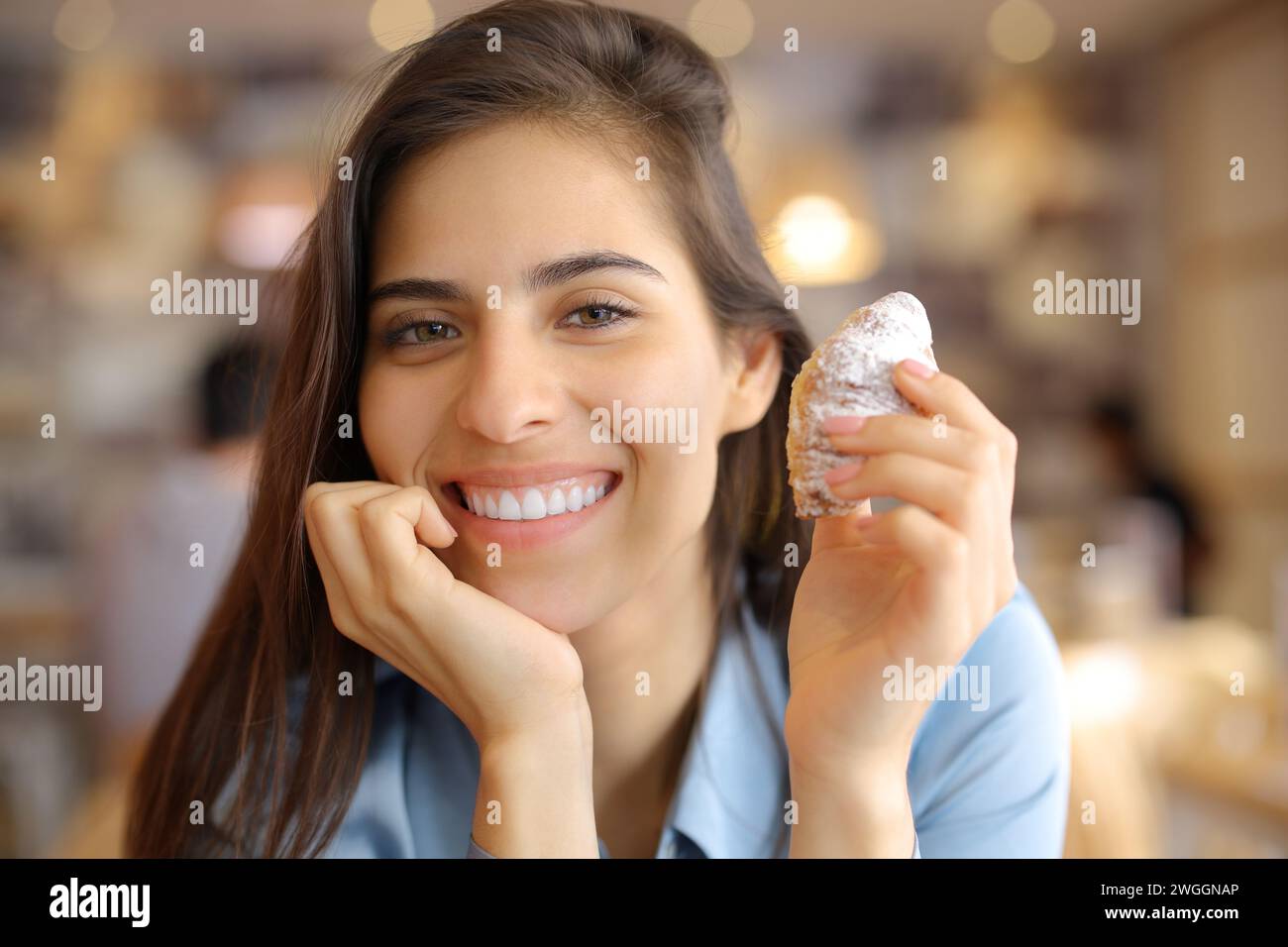 Femme heureuse souriante tenant une collation et regardant la caméra dans un intérieur de bar Banque D'Images