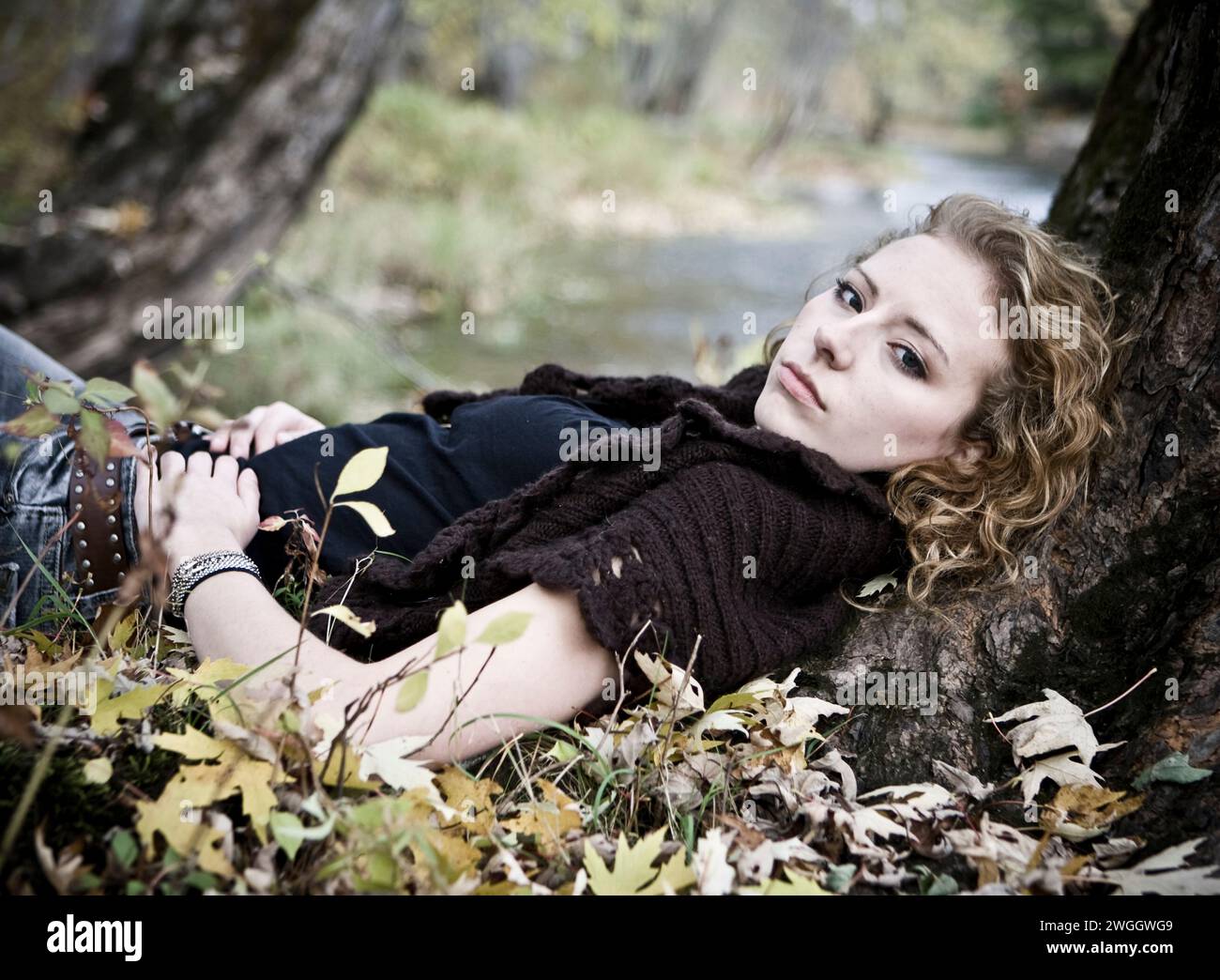 Portrait d'une jeune femme aux cheveux blonds bouclés couchés dans un lit de feuilles. Banque D'Images