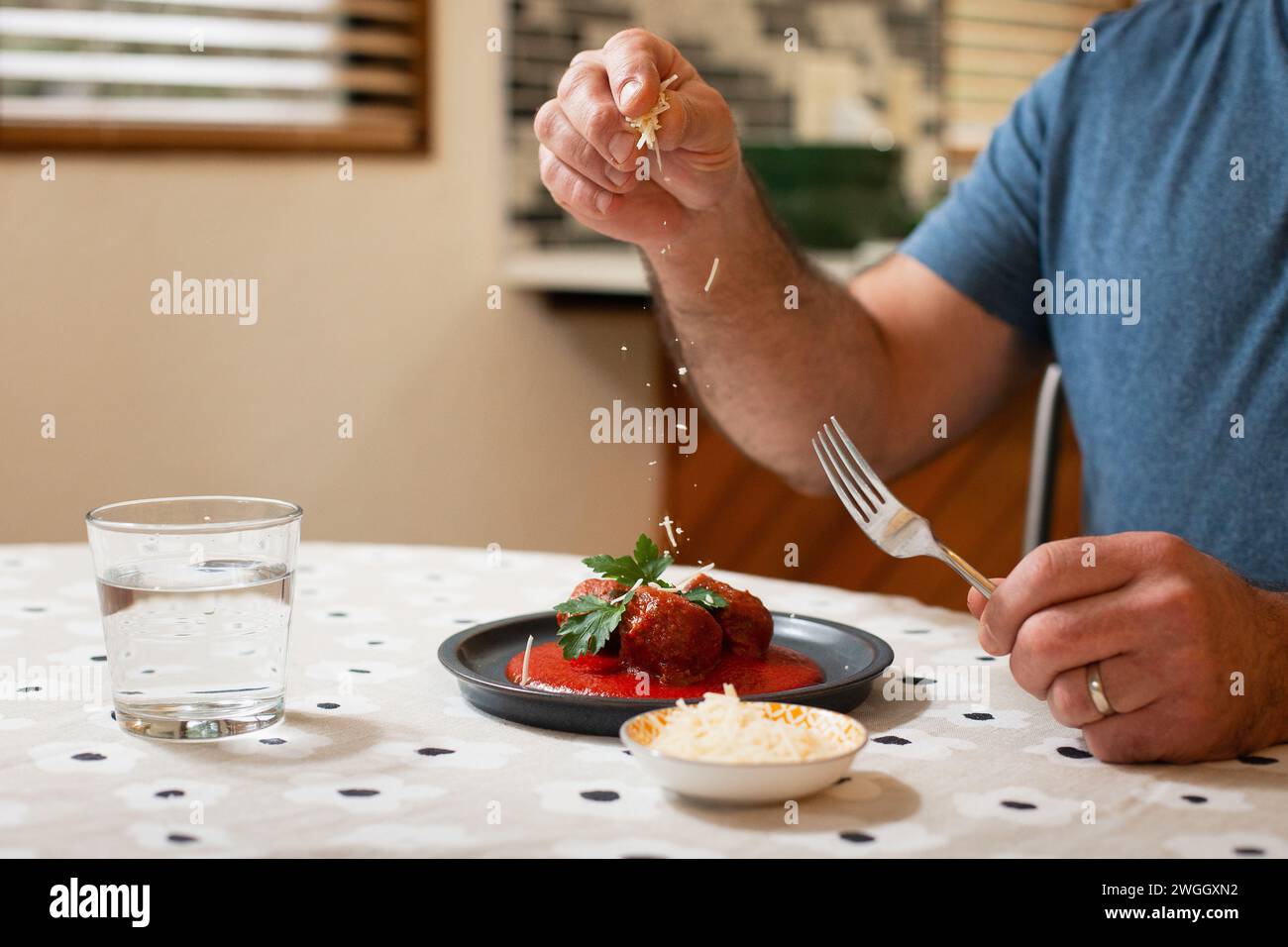 Homme saupoudrant du fromage sur les boulettes de viande et la sauce marinara Banque D'Images
